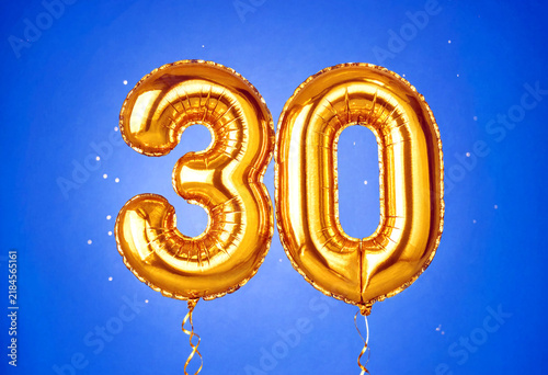 Golden number thirty foil balloons floating against a vibrant blue sky perfect for celebrations and anniversaries