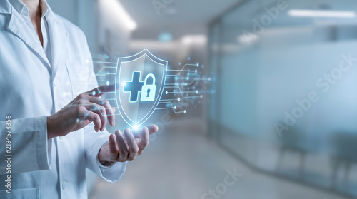 Healthcare professional using glowing digital shield icon for medical data security and patient privacy in a modern hospital setting, representing cybersecurity and encrypted health records.
