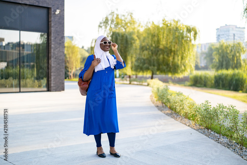 Принти на полотні A smiling African American Muslim woman wearing a white hijab and blue dress wal