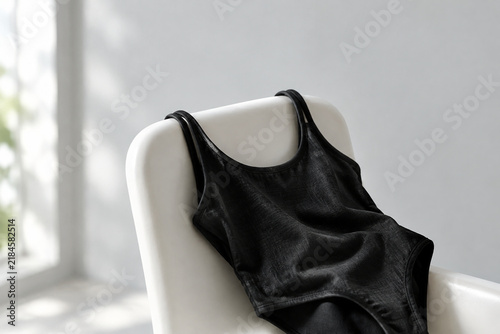 Black swimsuit draped on white chair, premium summer fashion concept