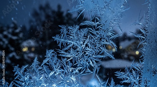 Intricate frost patterns on window glass with snowy winter night backg