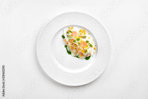 Gourmet scallop carpaccio with green oil, shaved fennel, and microgreens on a white ceramic plate. Top view studio photo.