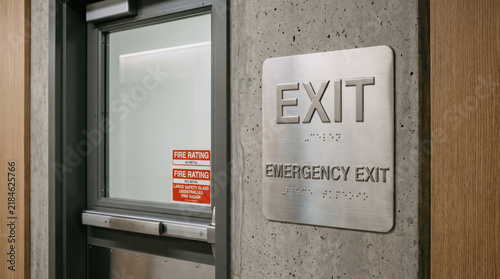 Emergency exit sign with Braille beside metal door in concrete hallway