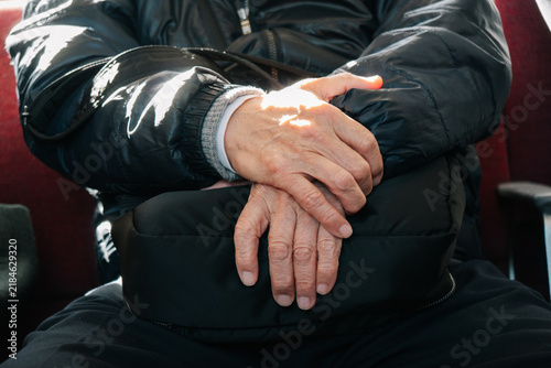 Close-up of an elderly man's hands resting peacefully on his black bag while sitting inside a commuter train carriage in Kyoto.