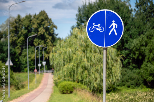 Sign shows bicycle and pedestrian path along a green area on a sunny day