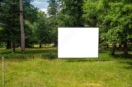 Large blank billboard stands in the park surrounded by trees and open grass