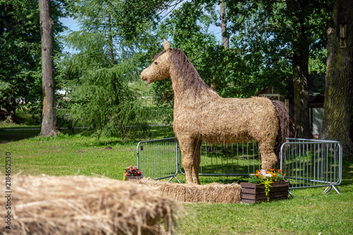 Straw horse sculpture stands in a park surrounded by trees during sunny daytime