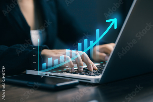 Business growth concept with person using a laptop and smartphone as a rising digital bar chart and arrow visualize revenue growth, financial performance, analytics, strategy, and success.