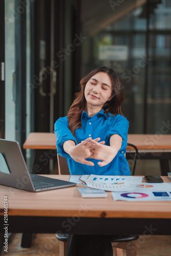 Asian businesswoman stretching arms and relaxing after finishing work at office desk