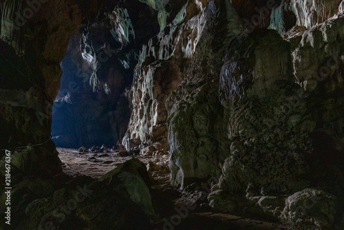 Dark interior of a natural limestone cave showing illuminated stalactite and stalagmite rock formations.