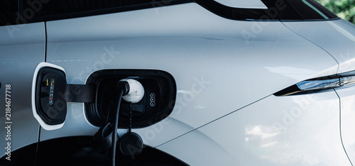 Person plugging in EV charging cable to white electric vehicle for sustainable energy transport.
