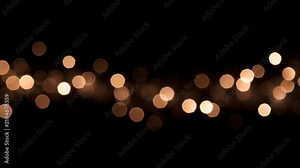 Obraz premium Golden bokeh lights on a black background. Horizontal band of blurred festive string lights. Abstract glowing holiday overlay.