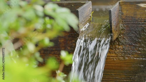 Fresh water flowing out of wooden box by green bush outdoors