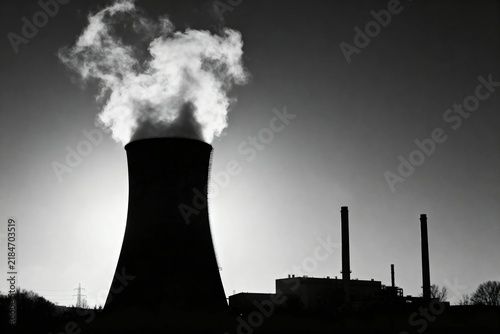 Bild auf Leinwand Silhouette of a cooling tower emitting steam against a dark sky, with industrial