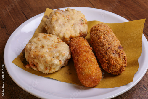 Bild auf Leinwand Plate of assorted Italian fried street food including crispy breaded croquettes and golden fritters, served on rustic paper over a wooden restaurant table