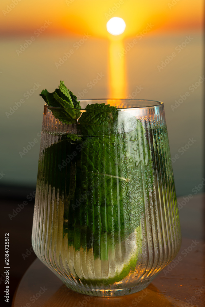 Obraz premium Mojito lemonade with lime and fresh mint overlooking the sea at sunset