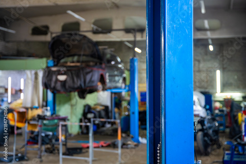 Bild auf Leinwand Car raised on vehicle lift with open hood inside auto repair shop
