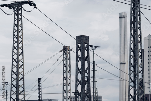 Overhead power lines and railway infrastructure form a dense industrial pattern of pylons and utility structures beneath a pale urban sky
