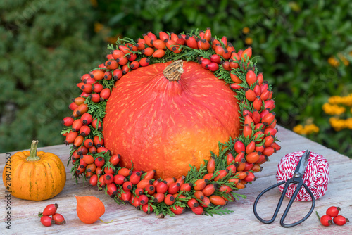 Herbst-Arrangement mit Kranz aus Hagebutten und Thujazweigen und Kürbissen