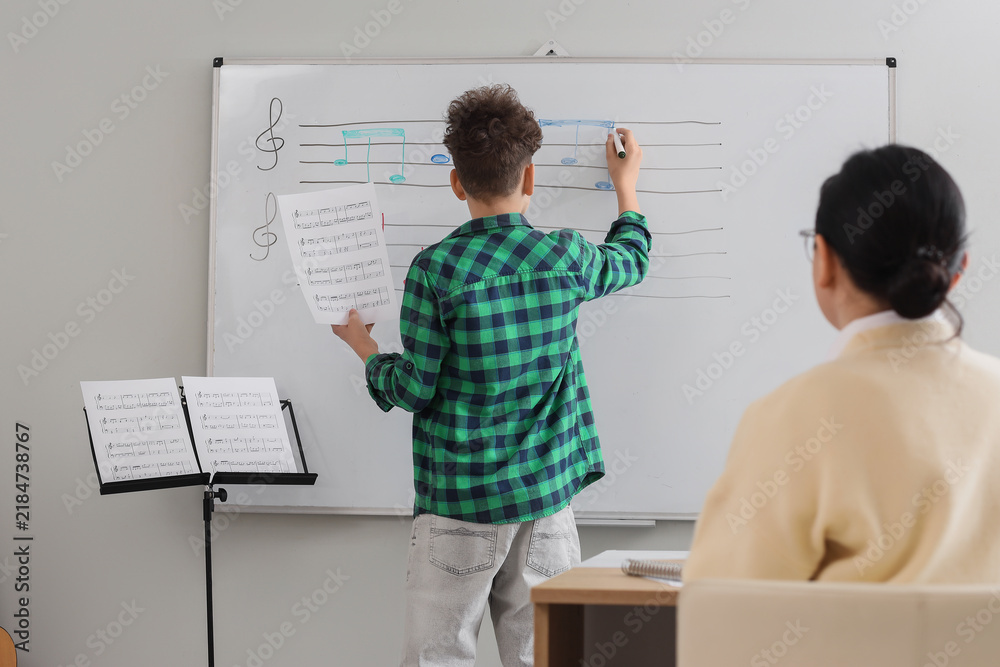 Obraz premium Teenage boy writing music notes on whiteboard in classroom, back view