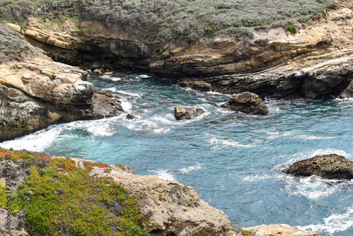 Фотография Dramatic rocky cove on the California coast, where turquoise Pacific Ocean water and foaming waves flow between weathered coastal rock formations