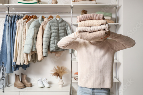 Young woman with folded winter clothes in wardrobe