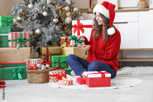 Young woman in Santa hat with Christmas gift sitting at home