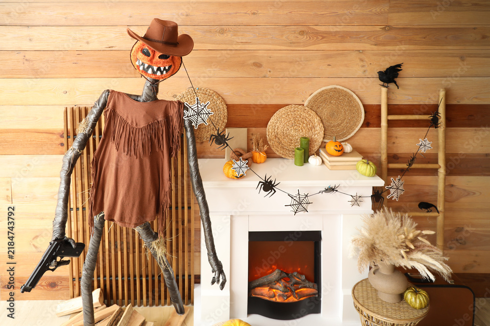 Fototapeta premium Interior of festive living room with ladder, Spooky Halloween monster, coffee table and autumn decorations on fireplace