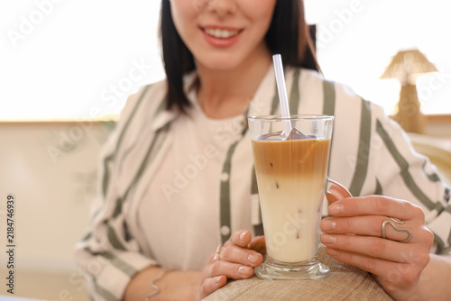 Young woman with glass of iced latte sitting on sofa at home, closeup