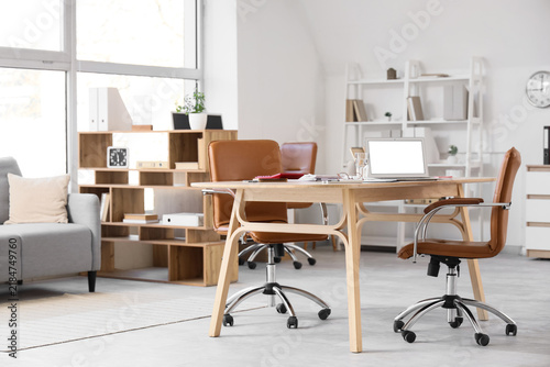Interior of light office with desk and shelf units
