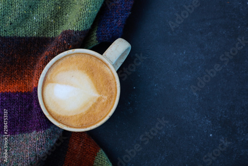 Hot tasty latte and warm woolen scarf. Seasonal coffee shop menu, autumn dink, cozy winter morning mood. Close up of objects on black background with copy space