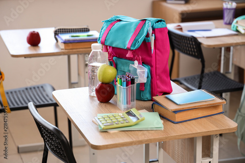 Apples with water bottle and backpack on desk in classroom