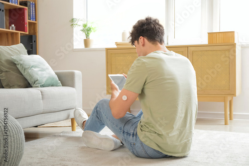 Diabetic young man with glucose sensor and tablet computer measuring blood su...
