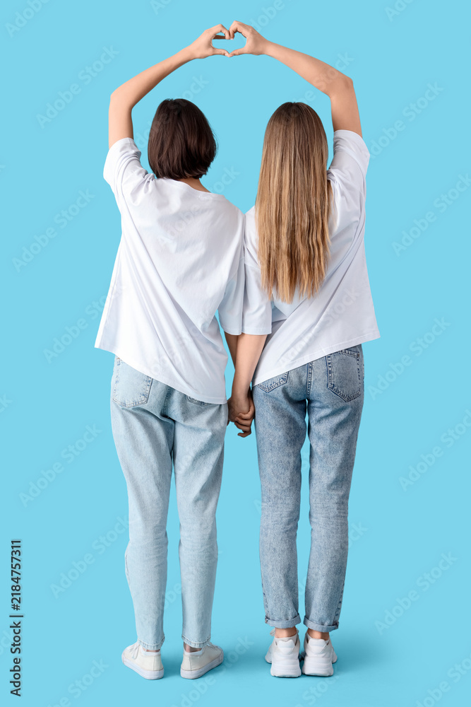 Naklejka premium Female friends making heart gesture on blue background, back view