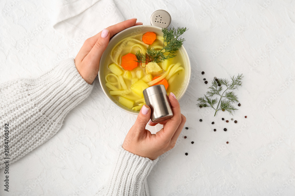 Obraz premium Woman adding spices into bowl with tasty chicken soup on white background