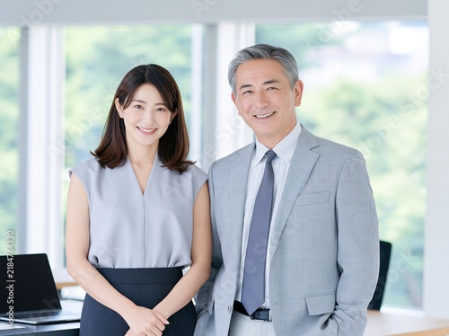 Obraz w ramie 開放的なオフィスで並んで立ち信頼の笑顔を見せる女性社員とシニア男性役員