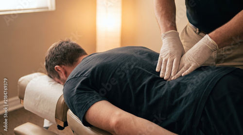 Chiropractor palpating patient lumbar spine during clinical back examination with gentle manual pressure and focused healthcare treatment in therapy room