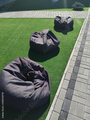 Row of grey bean bag chairs on green artificial lawn outdoors