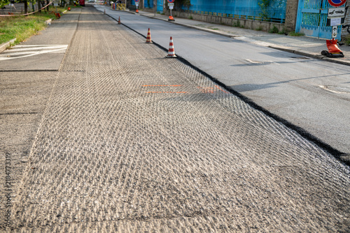 Milled asphalt road surface texture next to freshly laid smooth pavement, roadwork construction site with traffic safety cones, urban street resurfacing, infrastructure repair, selective focus