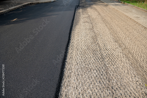 Milled asphalt road surface texture next to freshly laid smooth pavement, roadwork construction site with traffic safety cones, urban street resurfacing, infrastructure repair, selective focus