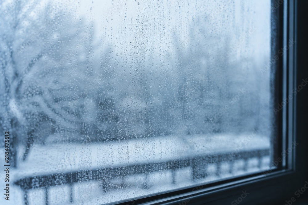 Obraz premium Fogged window glass with condensation drops overlooking snowy winter landscape
