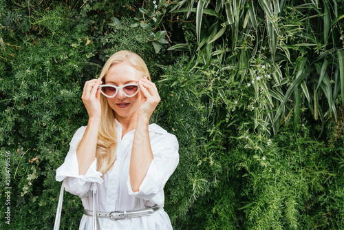 Blonde woman posing with cat eye sunglasses against green wall