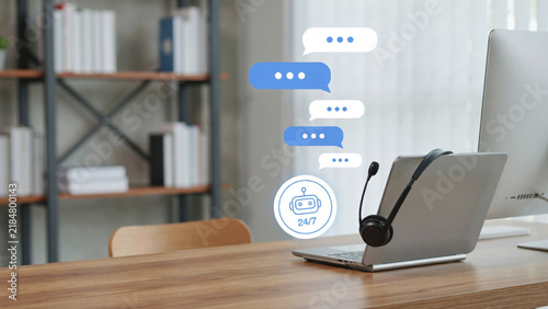 Laptop with headset and chatbot icon during remote work on a desk with bookshelves background
