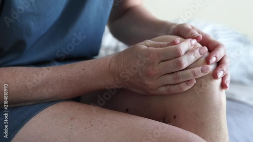 Closeup of unrecognizable female fingers massaging aching knee joint while sitting in bed