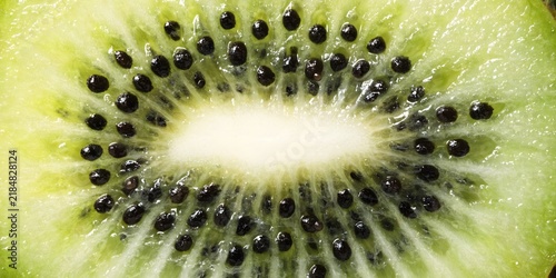 Extreme macro kiwi cross-section with radiating black seeds and vivid green fruit texture