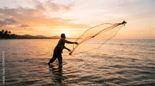Silhouette of a fisherman casting a net into the sea at sunset.