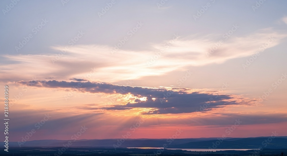 Obraz premium Serene sunset sky with dramatic clouds and golden rays over calm ocean horizon