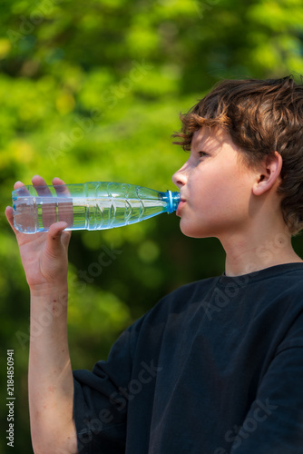 фотографія Young man refreshes himself by drinking water from a bottle on a warm summer day
