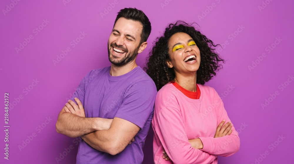 Obraz premium Happy young couple standing back-to-back laughing with arms crossed against a vibrant purple background.