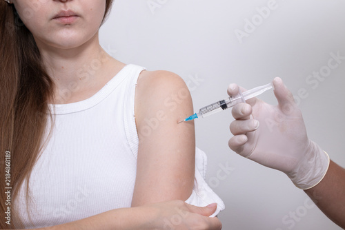 Doctor vaccinating woman by giving vaccine injection into exposed upper arm. Concept of HPV vaccination, cervical cancer prevention, influenza vaccination, hepatitis B vaccination, adult immunization.